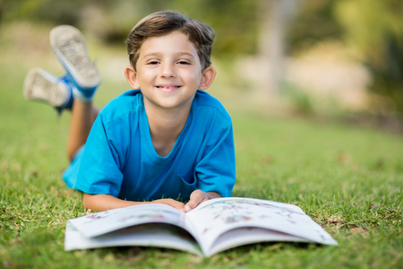 Portrait of young boy lying on grass with book in parkの写真素材