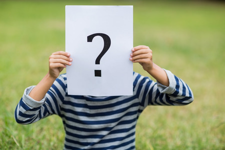 Boy in park covering his face with a placard that shows question mark sign