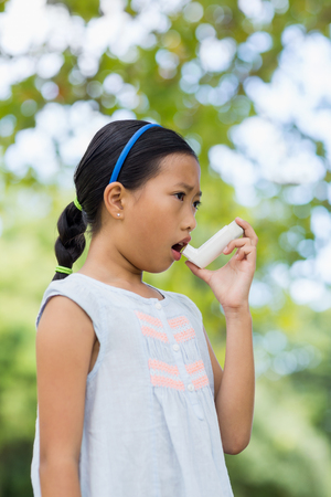 Girl using an asthma inhaler in the parkの写真素材