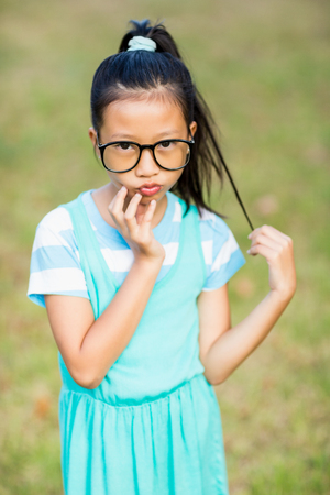 Portrait of girl standing with hand on chin in parkの写真素材