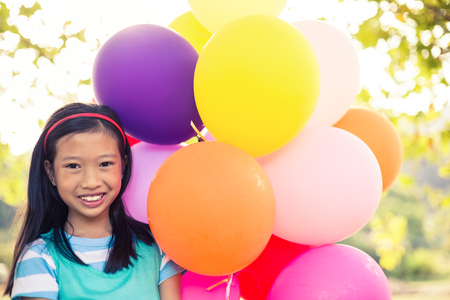 Portrait of smiling girl holding balloons in park on a sunny dayの写真素材
