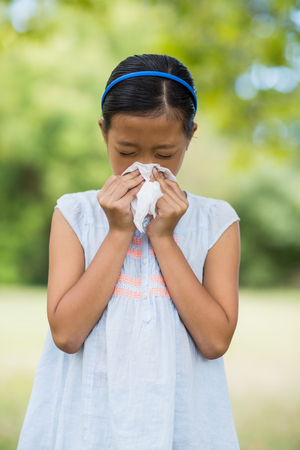 Girl blowing her nose with handkerchief while sneezing in the parkの写真素材