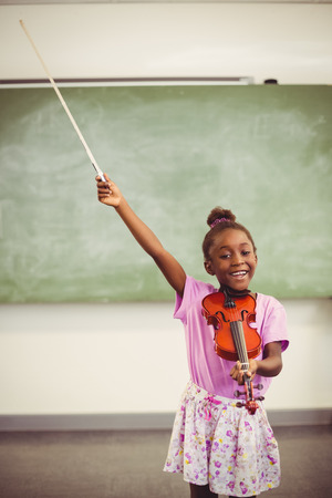 Portrait of smiling schoolgirl playing violin in classroom at schoolの写真素材