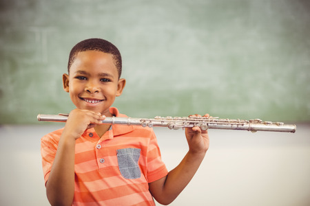 Portrait of smiling schoolboy playing flute in classroom at schoolの写真素材
