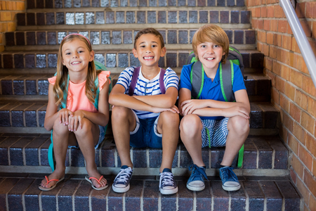 Portrait of smiling school kids sitting together on staircase at schoolの写真素材