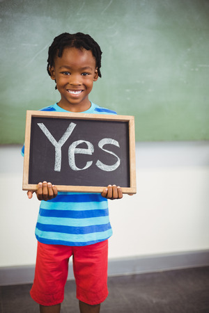 Smiling schoolboy holding a slate in classroom which reads yesの写真素材