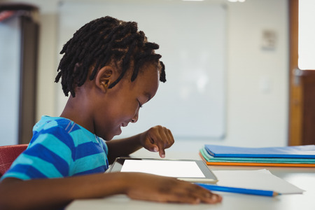 Schoolboy sitting on chair and using digital tablet in classroom at school
