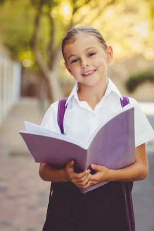 Portrait of happy schoolgirl reading book in campus at schoolの写真素材