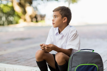 Thoughtful schoolboy sitting alone in campus at schoolの写真素材