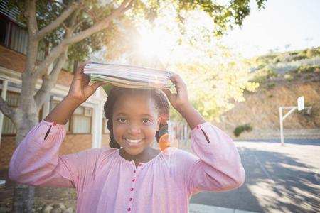 Schoolgirl carrying books on her head in campus at schoolの写真素材