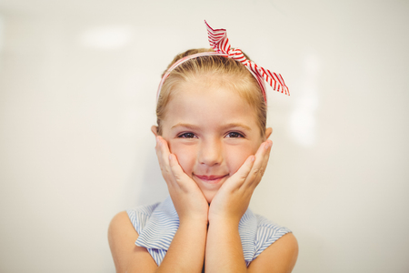 Portrait of cute smiling girl posing at camera in classroom at schoolの写真素材