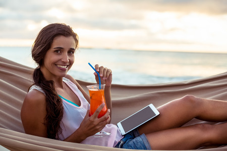 Portrait of woman holding mocktail while relaxing on a hammock on the beachの写真素材