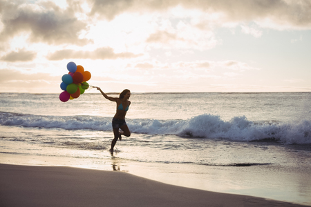Woman running with the balloon on the beachの写真素材