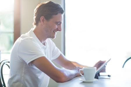 Smiling man sitting in restaurant using digital tableの写真素材