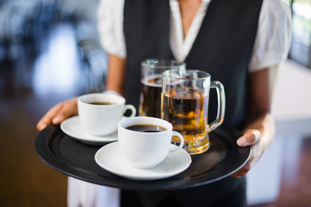 Mid section of waitress holding serving tray with coffee cup and pint of beer in restaurantの写真素材