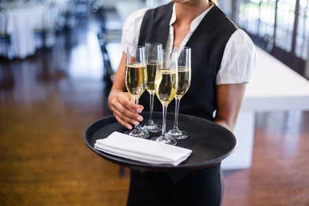 Mid section of waitress holding serving tray with champagne flutes in restaurant