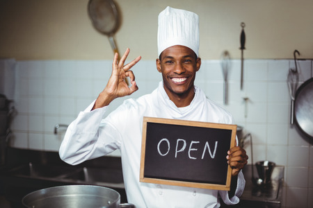 Smiling chef showing chalkboard with open sign in kitchenの写真素材