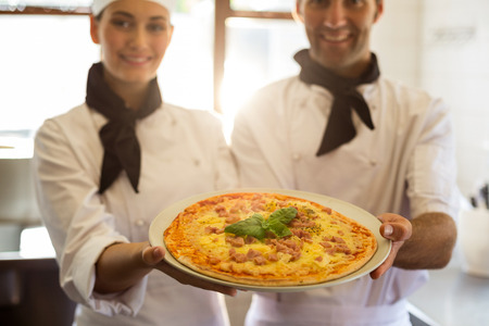 Portrait of two chef presenting a pizza in commercial kitchenの写真素材
