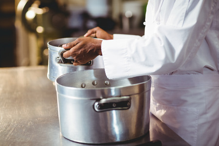 Mid section of chef holding cooking pot in kitchen
