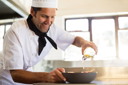 Chef pouring olive oil on meal in commercial kitchenの写真素材