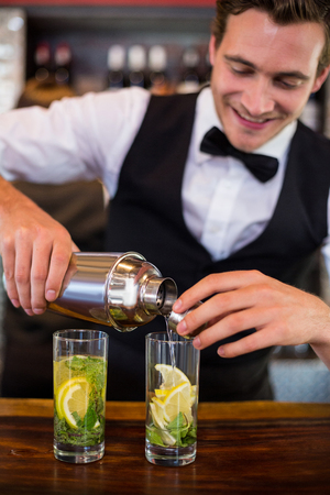 Bartender pouring a drink from a shaker to a glass on bar counter in barの写真素材