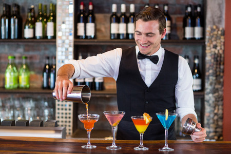 Bartender pouring a orange martini drink in the glass at barの写真素材