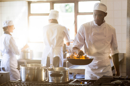 Chef tossing stir fry over large flame in commercial kitchenの写真素材