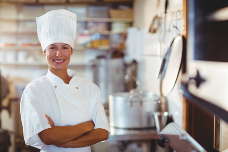 Portrait of happy chef standing with arms crossed in commercial kitchen