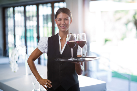 Portrait of smiling waitress holding a tray with glasses of red wineの写真素材