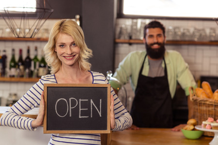 Portrait of two casual waiters holding a board written open in the bar