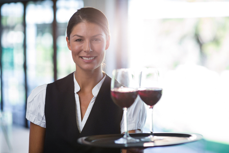Portrait of smiling waitress holding a tray with glasses of red wine