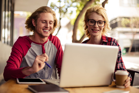Couple using a laptop on an outdoor terrace of a restaurantの写真素材