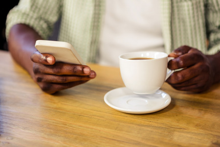 Hand holding a cup of coffee while using a smartphone in the restaurant