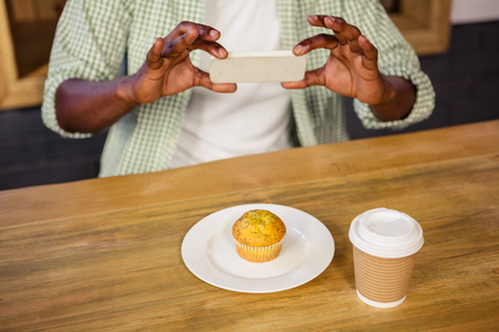 Man taking picture of a muffin in the cafeの写真素材