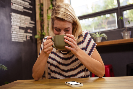 Woman drinking a hot beverage in the cafeの写真素材