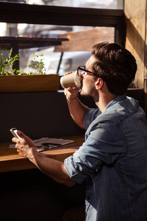Man drinking coffee and using smartphone in the cafeのeditorial素材