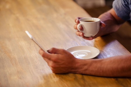 Cropped image of hipster man using smartphone while drinking cup of coffee at cafeの写真素材