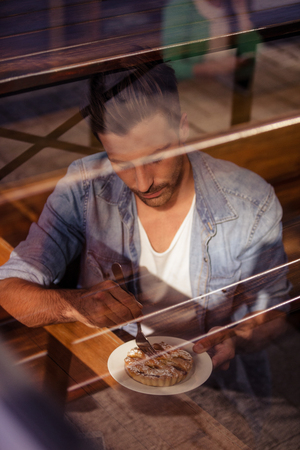 Facing view of hipster man eating pastries in coffee shopの写真素材