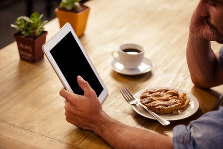 Cropped image of hipster man using tablet computer while eating and drinking at cafeの写真素材