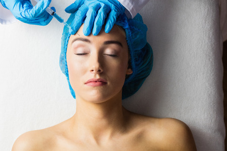 Woman receiving botox injection on her forehead in examination roomの写真素材