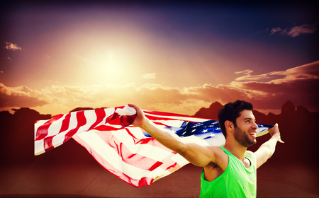 Happy sportsman holding a american flag  against composite image of landscapeの写真素材