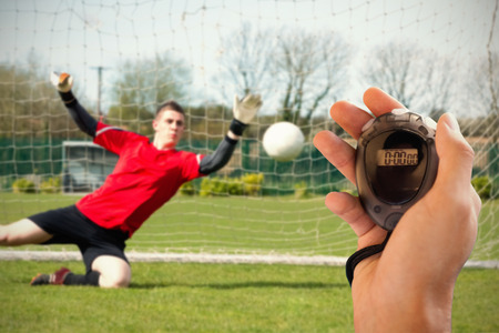 Composite image of coach is holding a stopwatch against goalkeeper in red ready to make a save