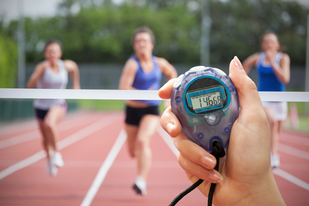 Composite image of a hand holding a timer against athletes racing towards finish lineの写真素材