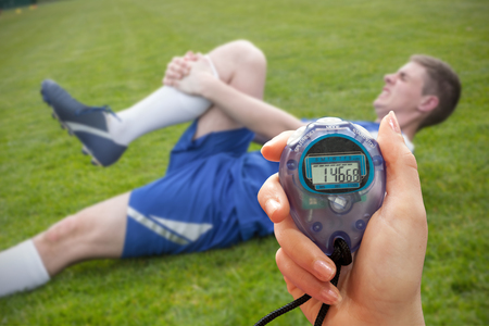 Composite image of a hand holding a timer against football player in blue lying injured on the pitch