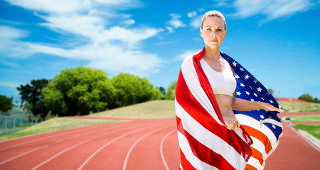 Portrait of sporty woman holding American flag against athletics field on a sunny dayの写真素材