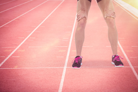 Tired athlete standing with hand on knee against focus of athletics trackの写真素材