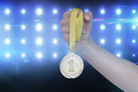 Athlete holding gold medal after victory against composite image of blue spotlightの写真素材