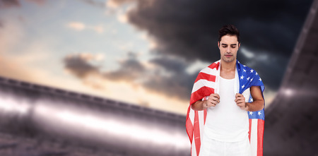 Athlete with american flag wrapped around his body against composite image of arena and cloudy skyの写真素材