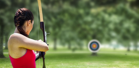 Rear view of sportswoman doing archery on a white background against park on sunny dayの写真素材