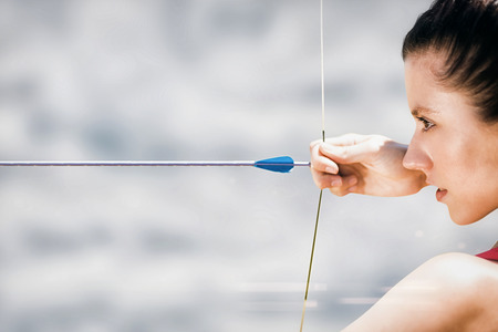 Close up of sportswoman practising archery on a white background against cloudy skyの写真素材